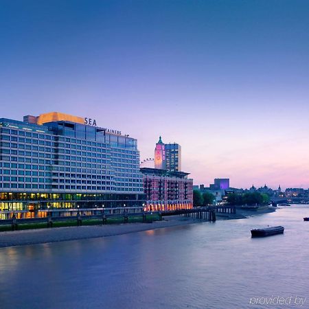 Hotel Sea Containers Londra Esterno foto The photo depicts a waterfront scene featuring a modern hotel building next to a river. The hotel has a sleek, contemporary design, with multiple stories and large windows reflecting the evening light. The sky transitions from a soft blue to warmer h