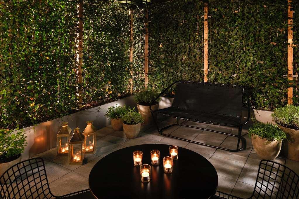 Hotel Sea Containers Londra Esterno foto The photo depicts a cozy outdoor seating area at night. There is a black metal bench situated against a backdrop of lush greenery, which creates a private and inviting atmosphere. A round black table in the center features several candles, providing 