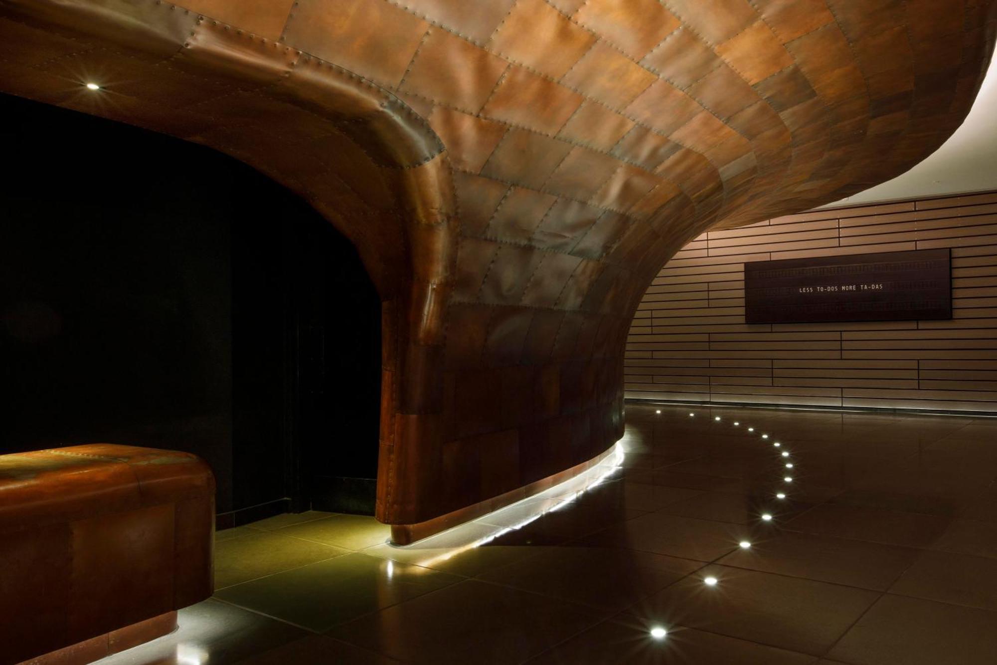 Hotel Sea Containers Londra Esterno foto The photo shows an interior space with a sleek, modern design. The walls appear to be made of a metallic material that has a warm, copper-like finish, creating a smooth and flowing appearance. The lighting is subtle, featuring small lights along the 