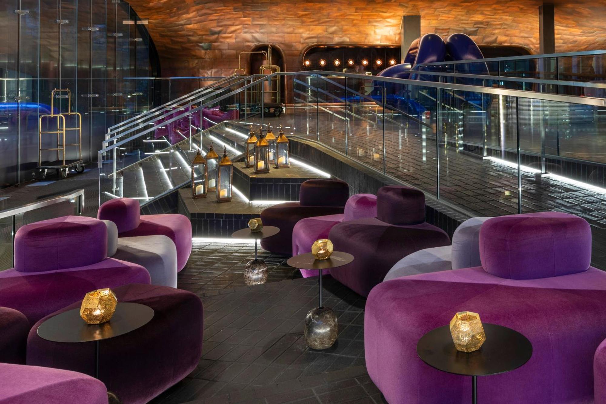 Hotel Sea Containers Londra Esterno foto The photo depicts a stylish interior space, likely a lounge or bar. It features modern, plush seating in shades of purple and velvet textures, arranged around small tables that hold decorative candle holders. The lighting is ambient, highlighting the