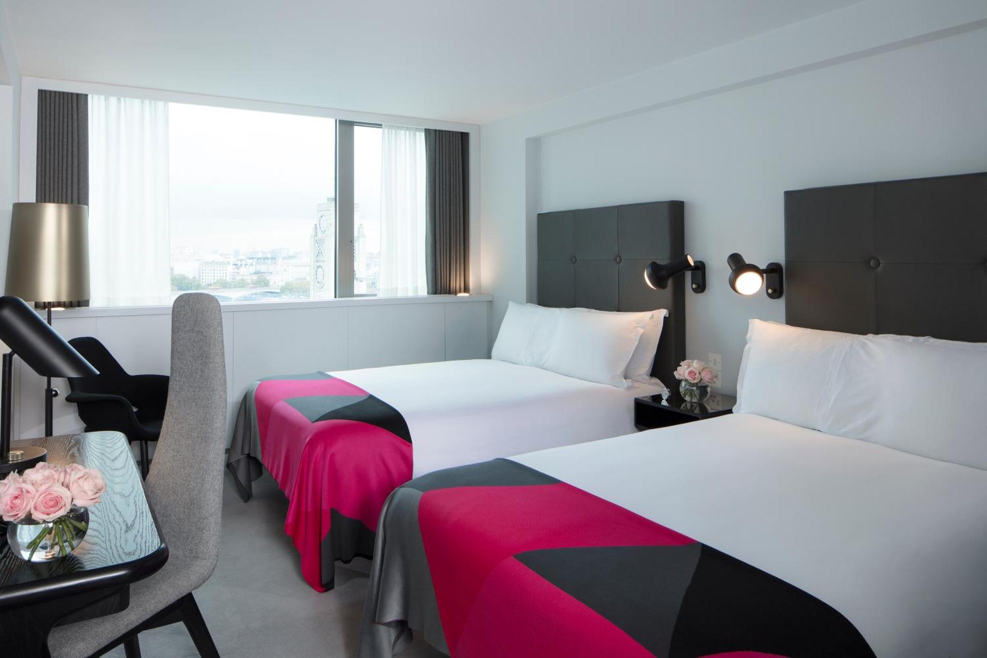 Hotel Sea Containers Londra Esterno foto The photo shows a modern hotel room featuring two beds with white linens and colorful bedspreads that have pink and black patterns. There are stylish black headboards behind each bed. A large window allows natural light to fill the space and offers a