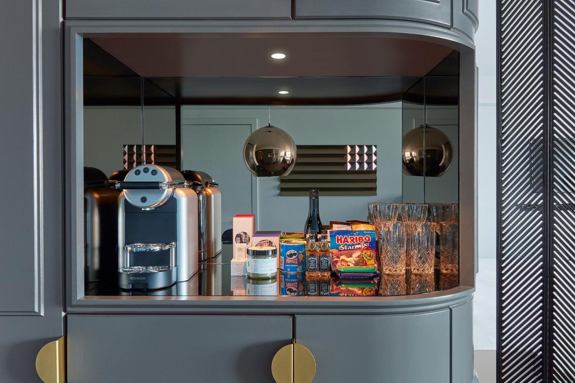 Hotel Sea Containers Londra Esterno foto The photo displays a modern kitchen nook with a sleek design. It features a coffee machine on the left, placed on a dark countertop. Next to it, there are several glass drinking glasses arranged neatly. Prominently displayed is a colorful box of snac