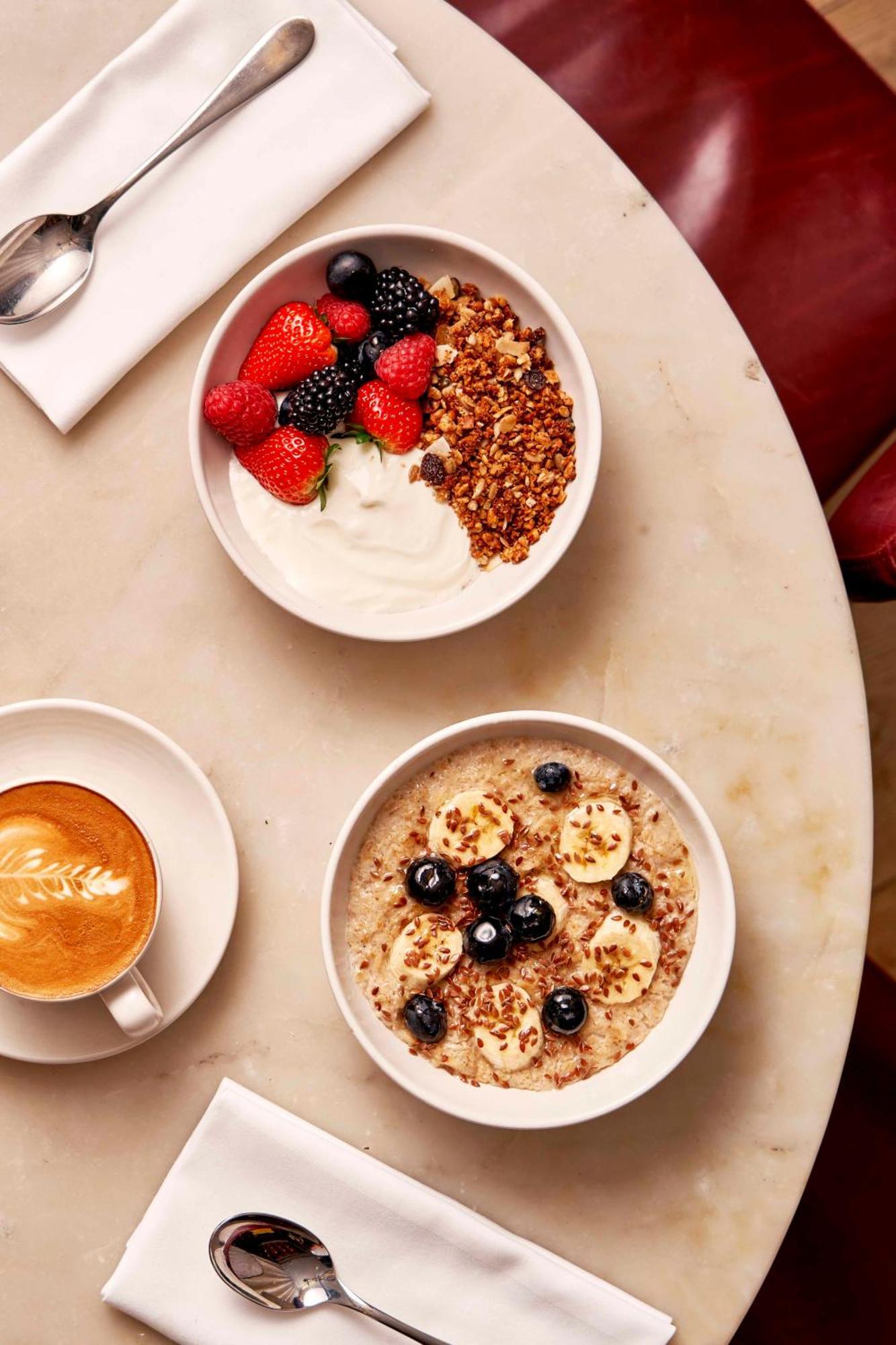 Hotel Sea Containers Londra Esterno foto The photo shows a delicious breakfast setting on a table. There are two bowls of food: one contains Greek yogurt topped with granola, mixed berries (like strawberries, blueberries, and blackberries), and another bowl features oatmeal topped with bana
