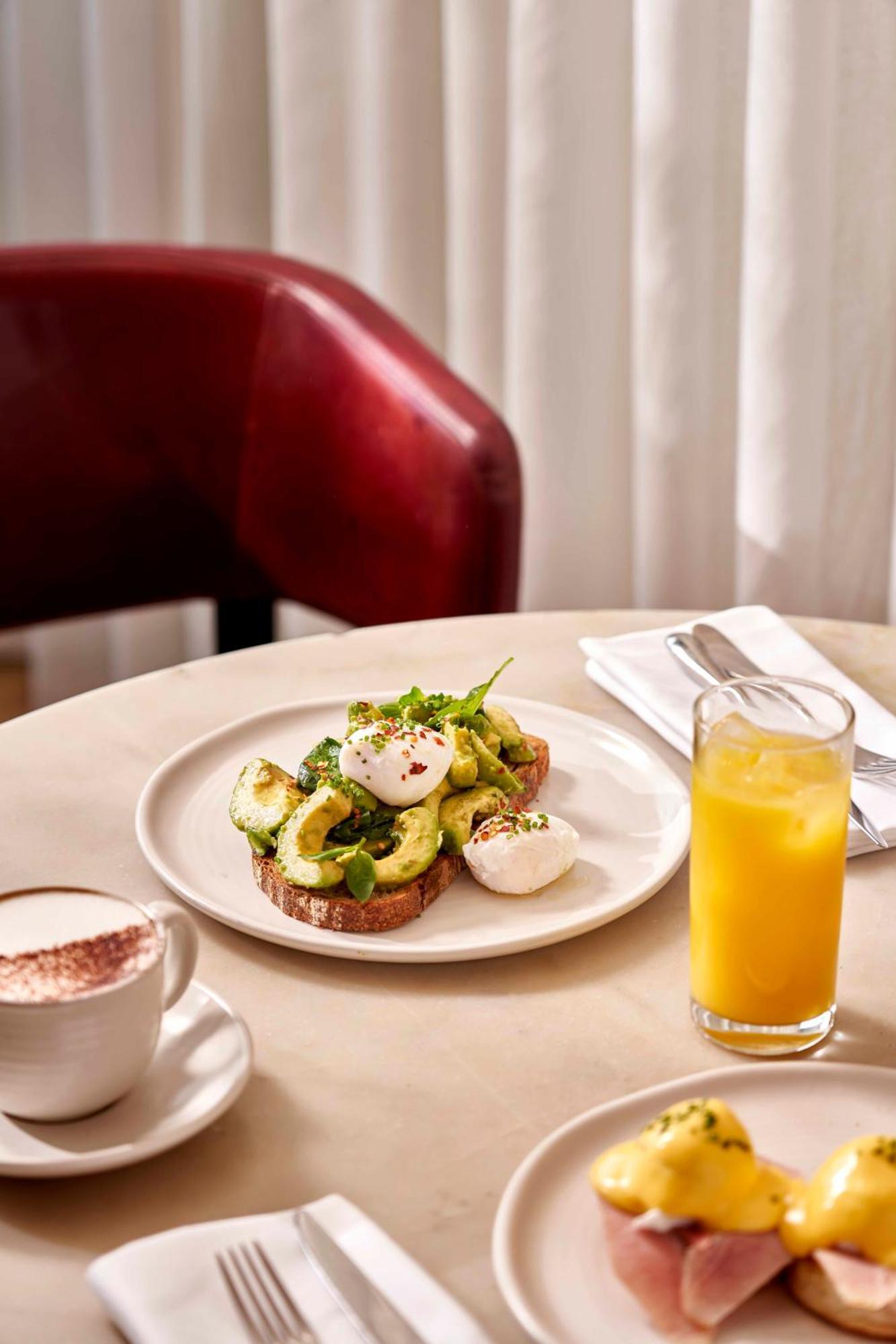 Hotel Sea Containers Londra Esterno foto The photo shows a plate of food featuring sliced avocado on toast, topped with poached eggs and garnished with herbs and spices. The toast appears to be whole grain. There's also a glass of orange juice on the side and a cup of coffee, possibly cappu
