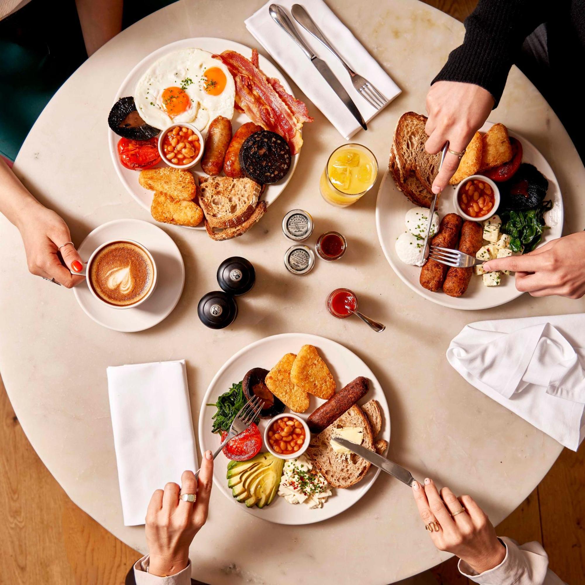 Hotel Sea Containers Londra Esterno foto The photo shows a beautifully set table with three plates of food, each featuring a variety of breakfast items. The dishes include:

1. **Main Plates**: Each plate contains a hearty breakfast spread, which includes items like eggs, bacon, sausages, b