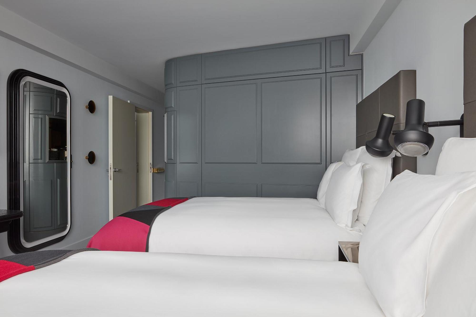 Hotel Sea Containers Londra Esterno foto The photo shows a hotel room with a contemporary design. It features two beds with white linens, complemented by vibrant pink and gray accents. The walls are painted in a soft gray color, creating a modern and minimalistic aesthetic. There is a styli