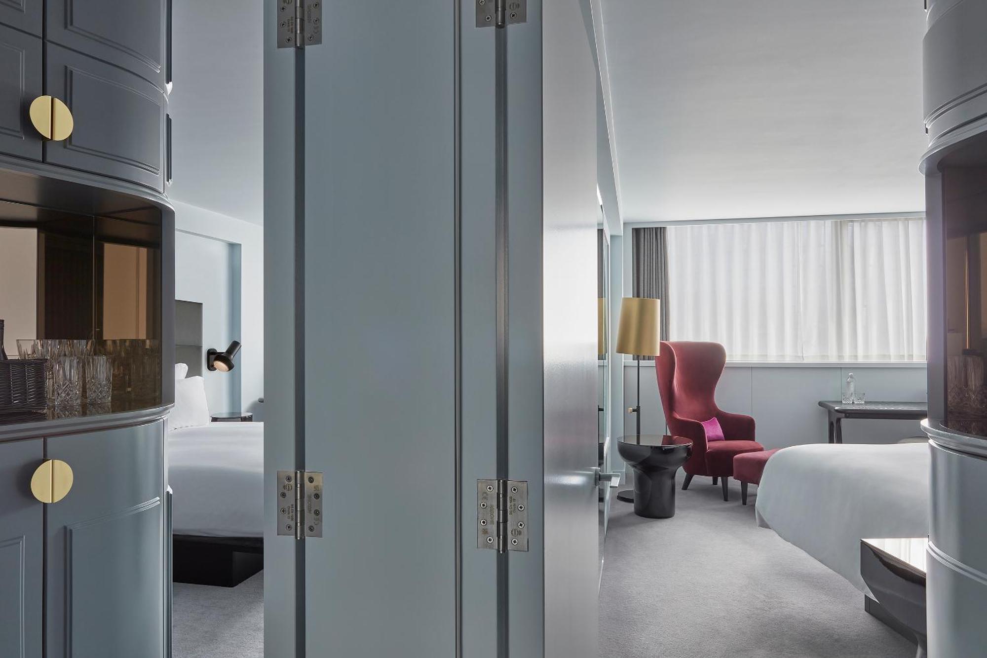 Hotel Sea Containers Londra Esterno foto The photo shows an interior space that appears to be a modern hotel room. The room is divided by a pair of large, grey doors that are slightly ajar. To one side, there are elements that hint at a welcoming, spacious ambiance, such as a bed with white