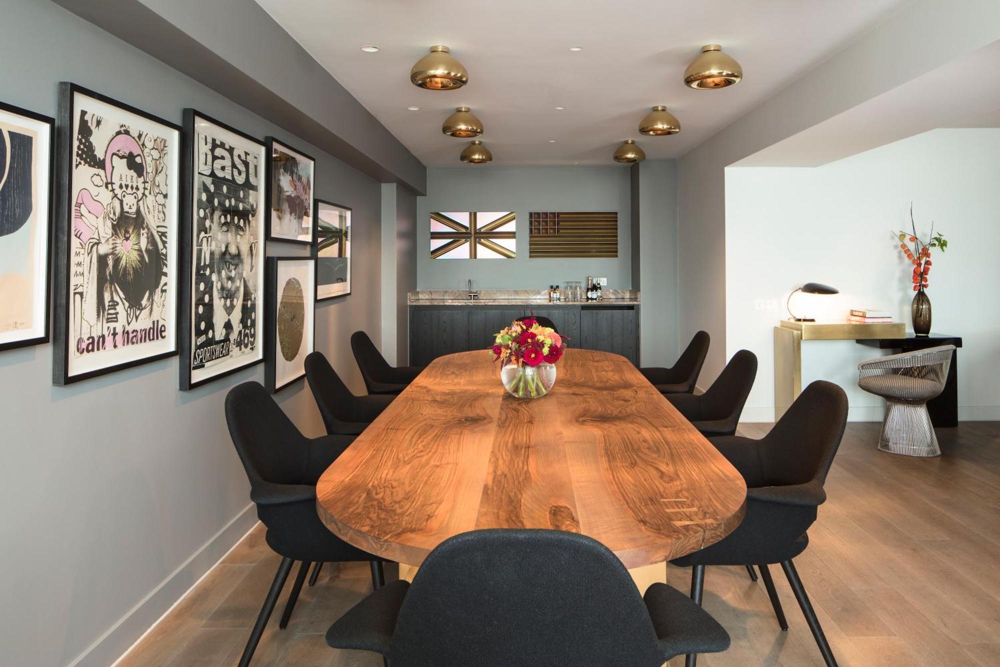 Hotel Sea Containers Londra Esterno foto The image depicts a modern dining or conference room. There is an elongated wooden table at the center, surrounded by black chairs. The walls are painted in a neutral gray color and adorned with several framed artworks, which include posters and abst