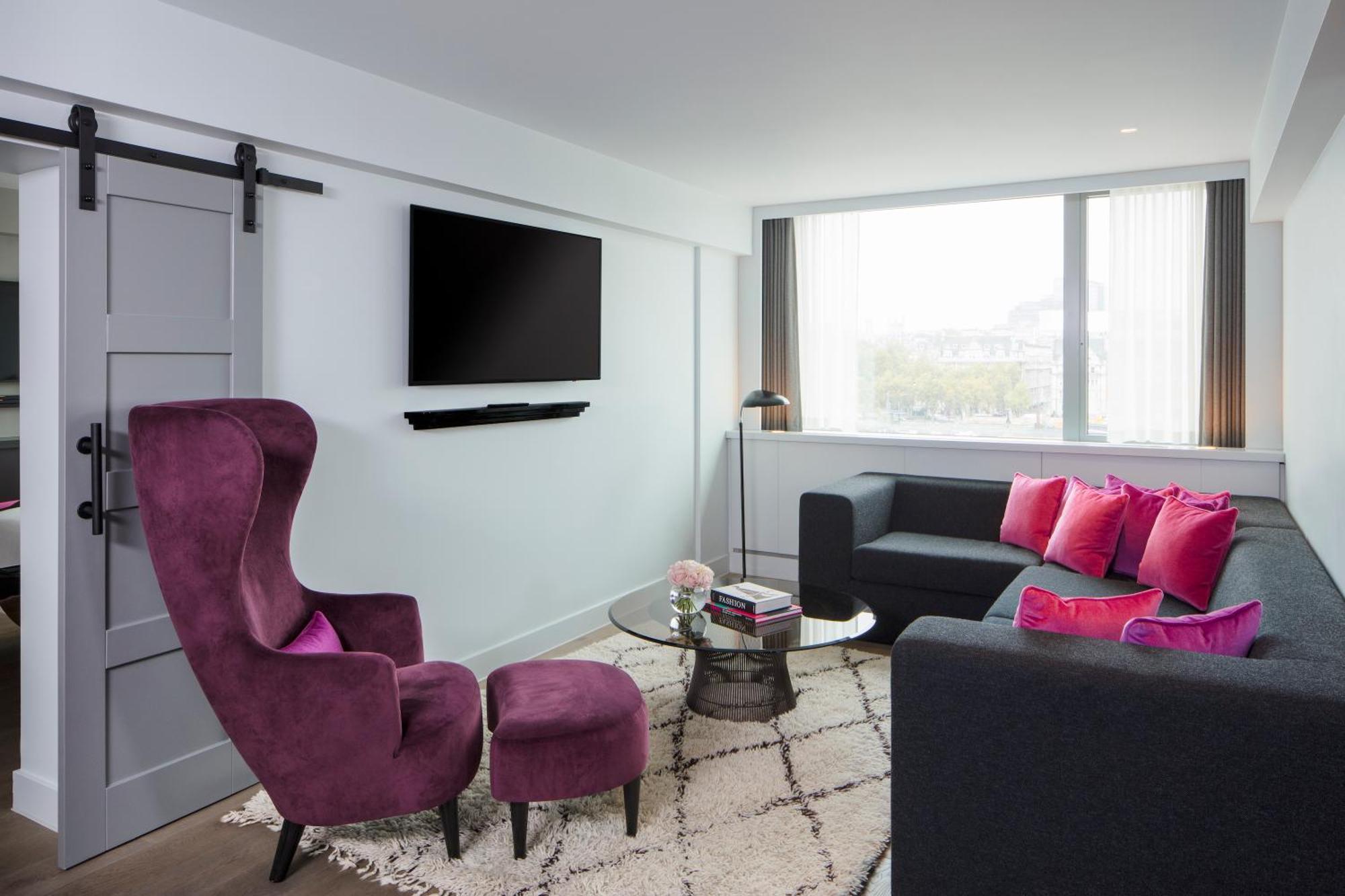 Hotel Sea Containers Londra Esterno foto The photo shows a modern living room with a clean and stylish design. There is a large window that allows natural light to fill the space. A comfortable dark sofa is accompanied by vibrant pink cushions, adding a pop of color. Next to the sofa is a r