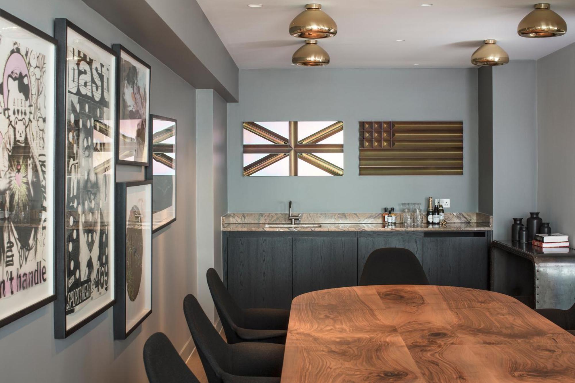 Hotel Sea Containers Londra Esterno foto The photo shows a modern interior space, likely a dining or meeting area. There is a large wooden table in the foreground surrounded by black chairs. On the walls, several framed artworks are displayed, with a focus on two pieces that represent flags