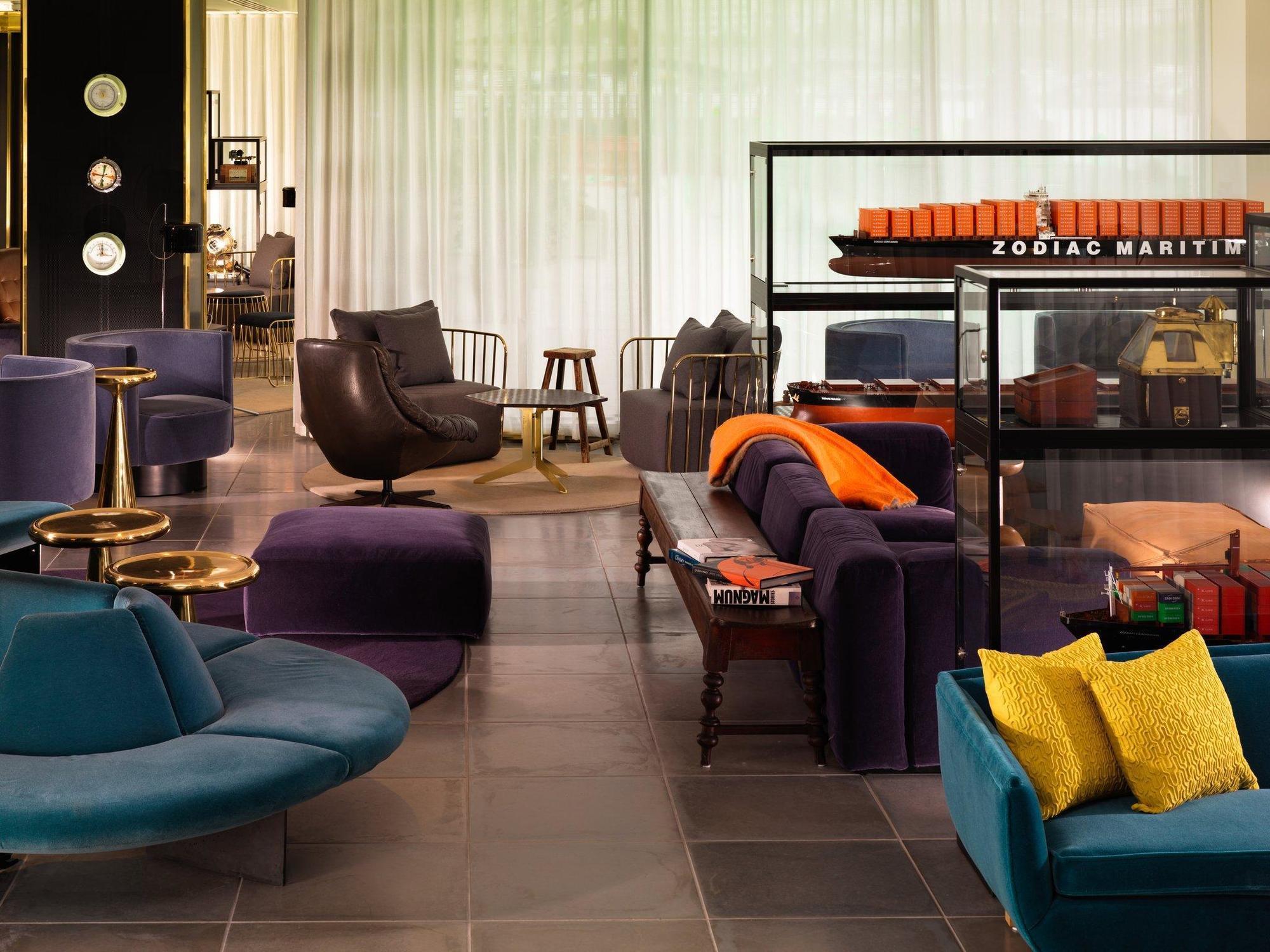 Hotel Sea Containers Londra Esterno foto The photo depicts a modern interior space, likely a lounge or lobby area. The design features a variety of stylish furniture pieces, including a curved blue sofa, purple armchairs, and a sleek black chair. There is a mix of coffee tables and side tab