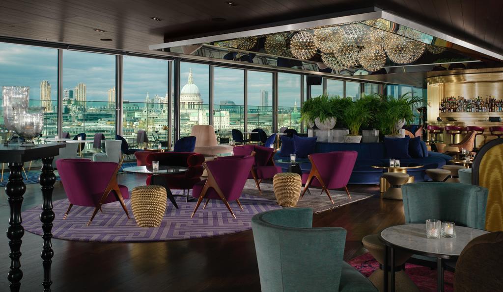 Hotel Sea Containers Londra Esterno foto The image depicts a stylish interior of a high-rise lounge or bar, featuring large windows that provide a panoramic view of an urban skyline. The decor is modern and elegant, with a mix of seating options, including plush chairs in deep purple and te