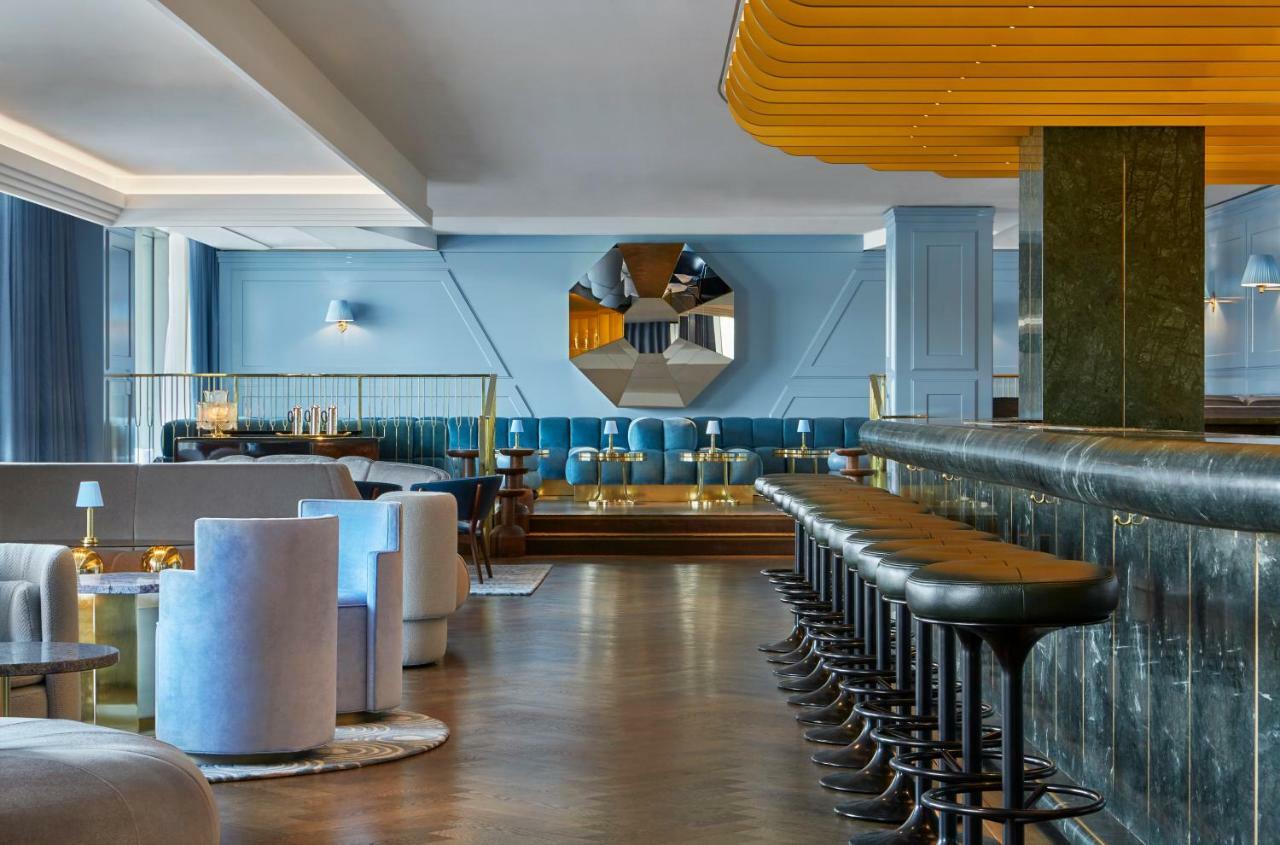 Hotel Sea Containers Londra Esterno foto The photo displays a modern and stylish bar or lounge area. The interior features a combination of soft blue walls and elegant furnishings. There are circular seating arrangements in light colors, creating a cozy atmosphere. A long bar counter made o
