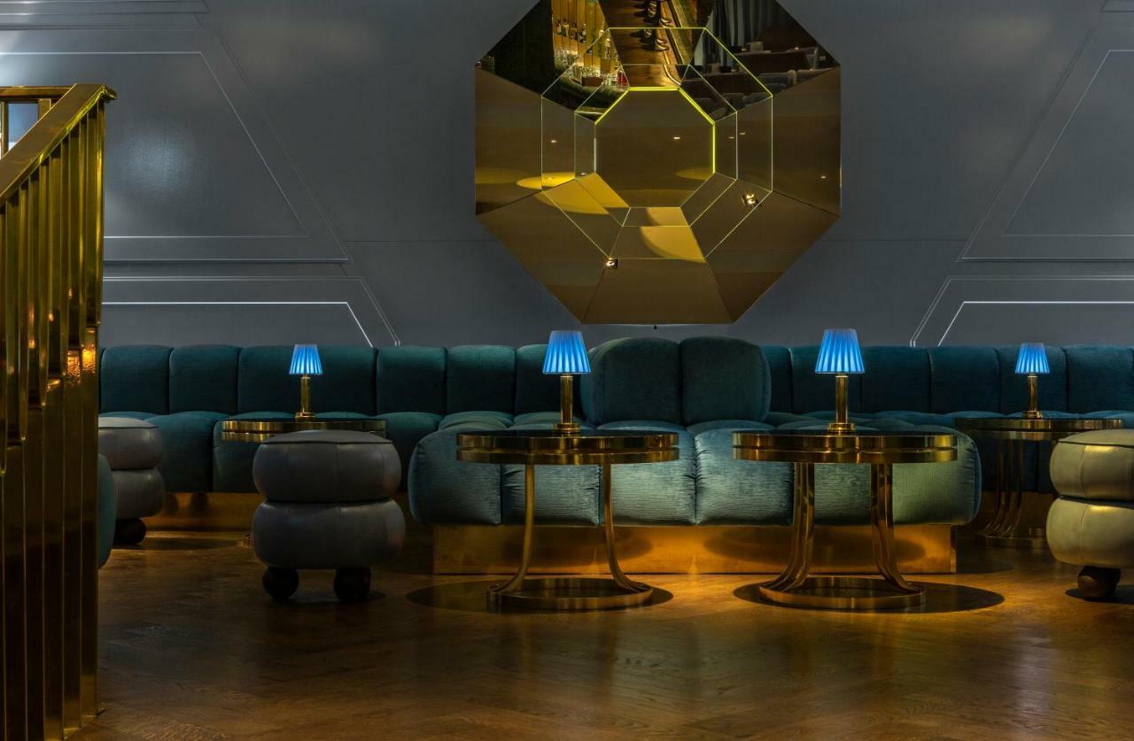 Hotel Sea Containers Londra Esterno foto The photo showcases a stylish, modern lounge or seating area. It features a curved, plush couch in a soft teal color, complemented by golden accents. There are several circular tables with shiny metallic bases, each topped with small blue lamps that 