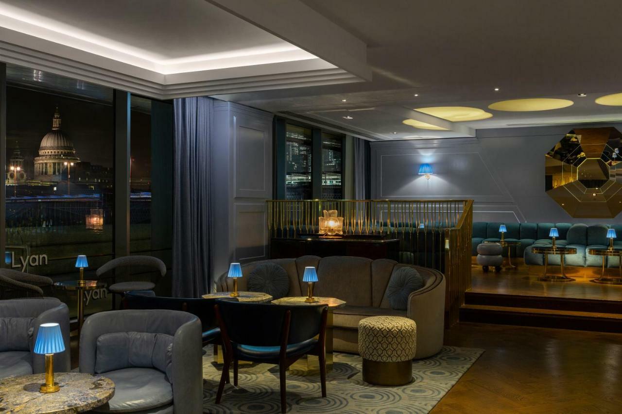 Hotel Sea Containers Londra Esterno foto The photo depicts a stylish interior of a lounge or bar. The space features elegant seating arrangements, including plush sofas and chairs, with small tables placed throughout. Ambient lighting is provided by small blue lamps on the tables and recess