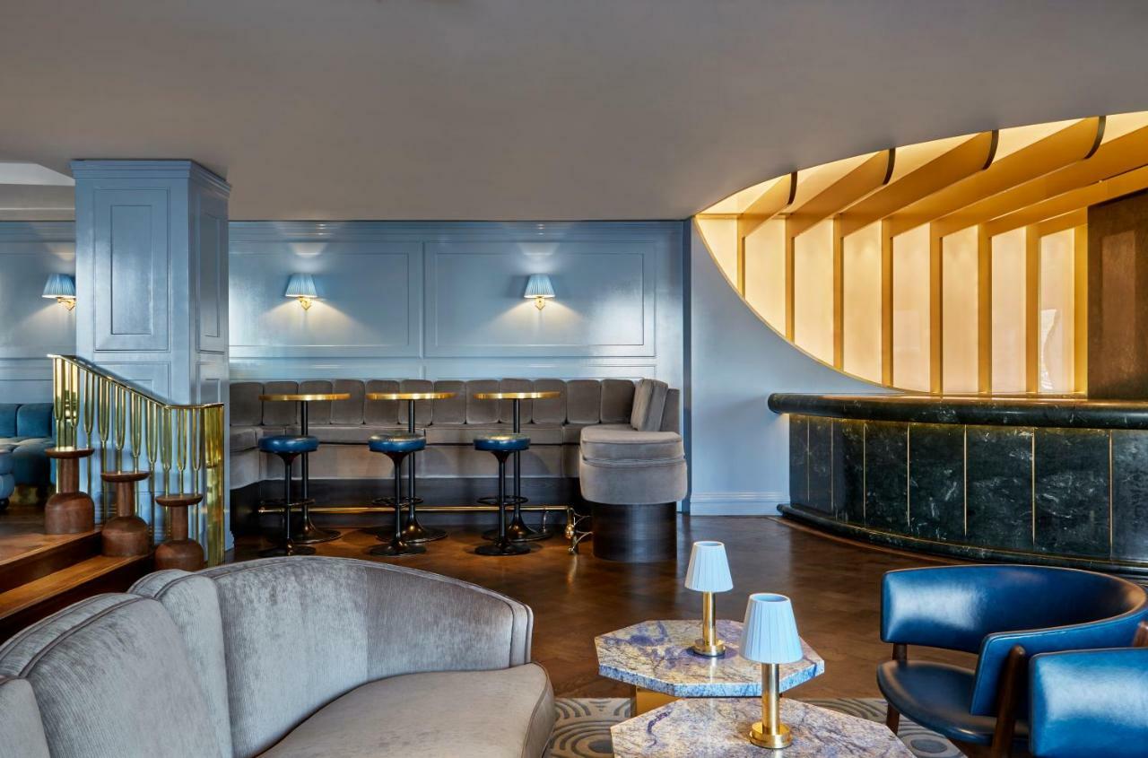 Hotel Sea Containers Londra Esterno foto The photo shows an elegantly designed interior space, likely a bar or lounge. The area features a modern seating arrangement with a mix of comfortable sofas and bar stools. The walls are painted in a soft blue color, complemented by wooden accents an